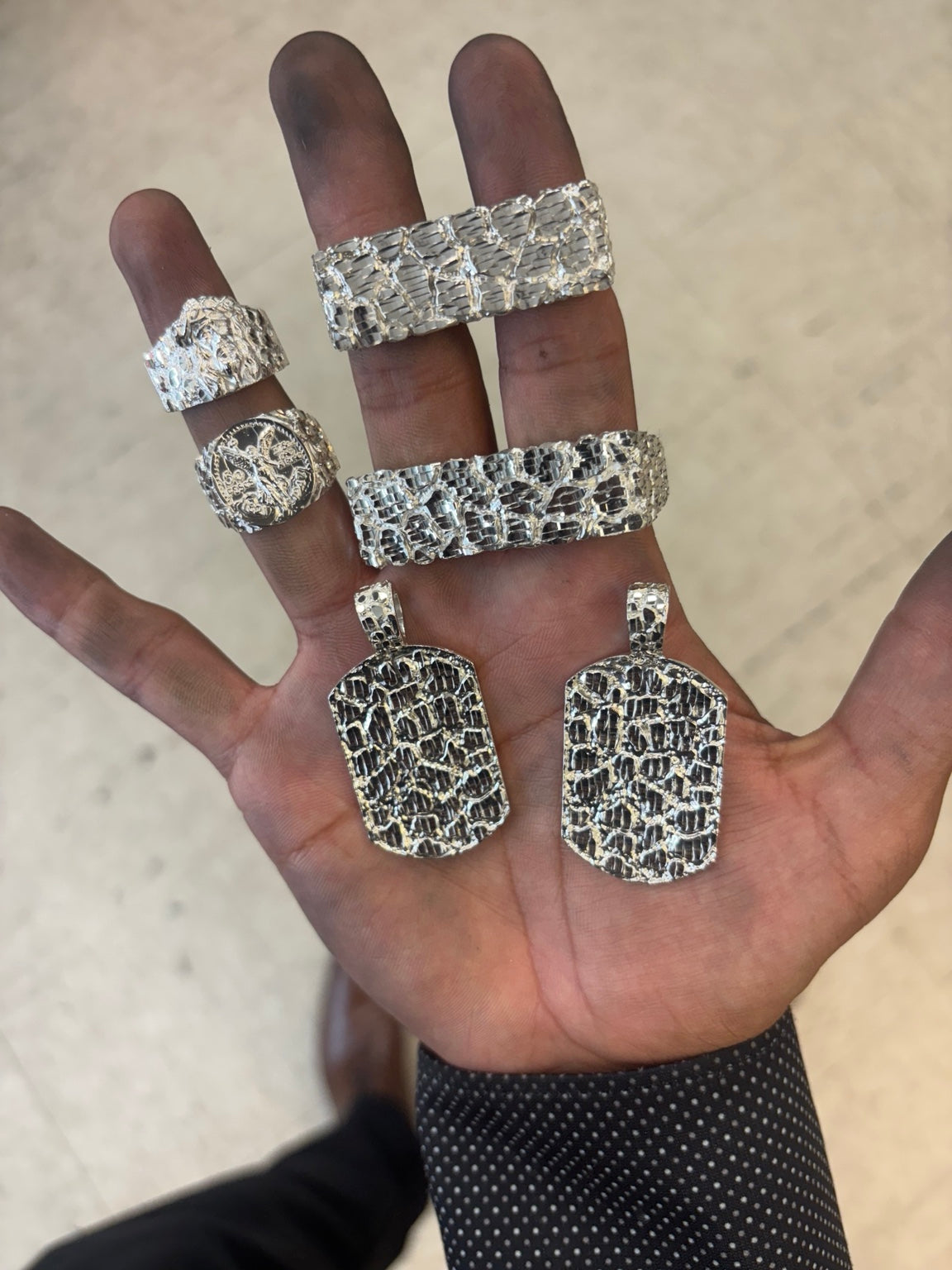 Hand holding finished silver rings and nugget pendants from Dโs Custom Jewelry